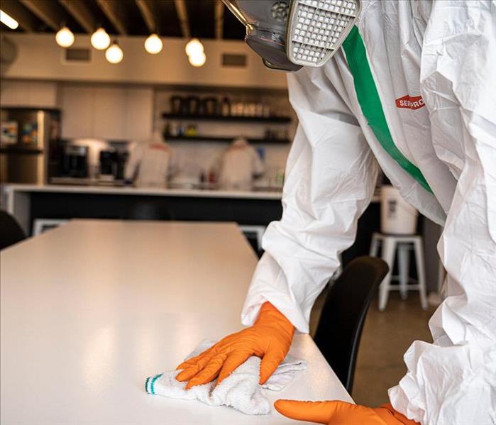SERVPRO worker in full PPE disinfecting table in restaurant